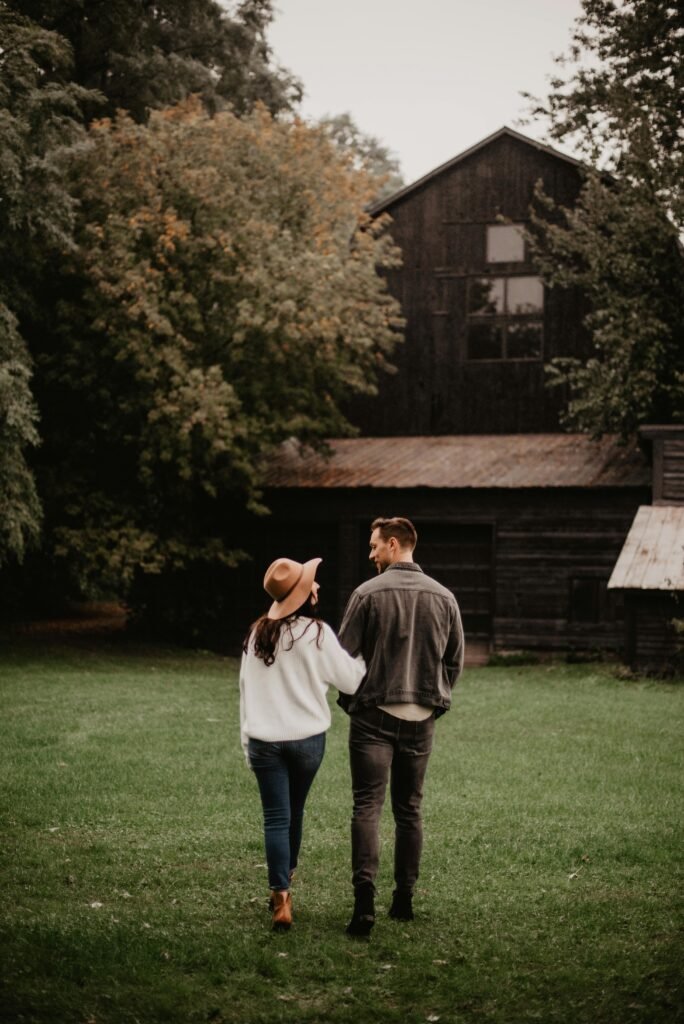 A couple walks through a grassy area towards a rustic barn, capturing a romantic autumn ambiance.