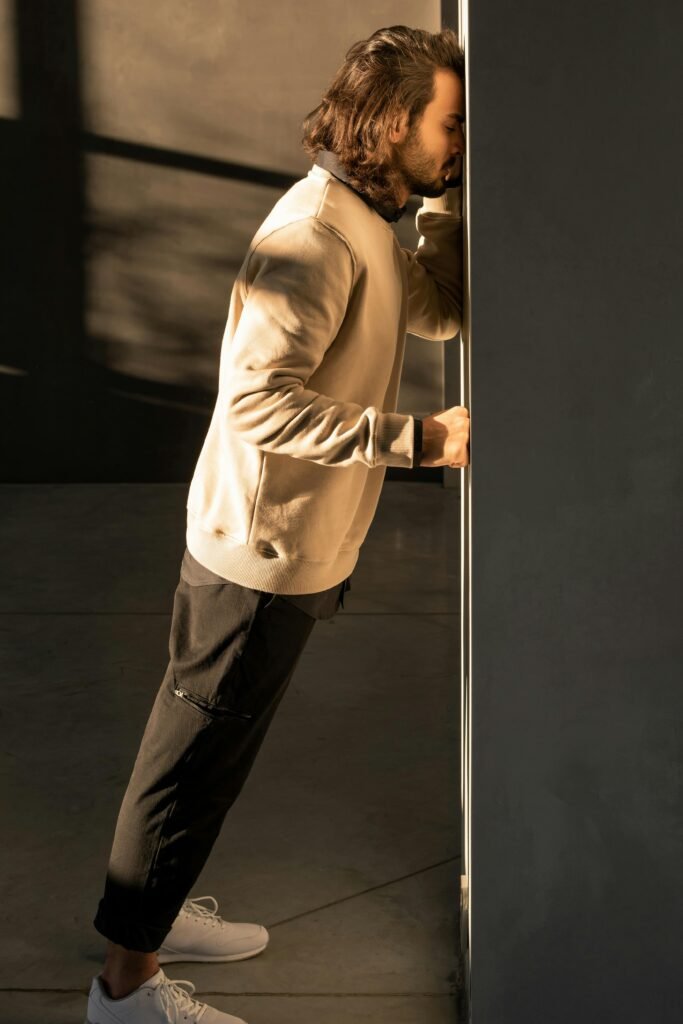 A man in casual attire showing frustration by leaning against a wall in a dark room.