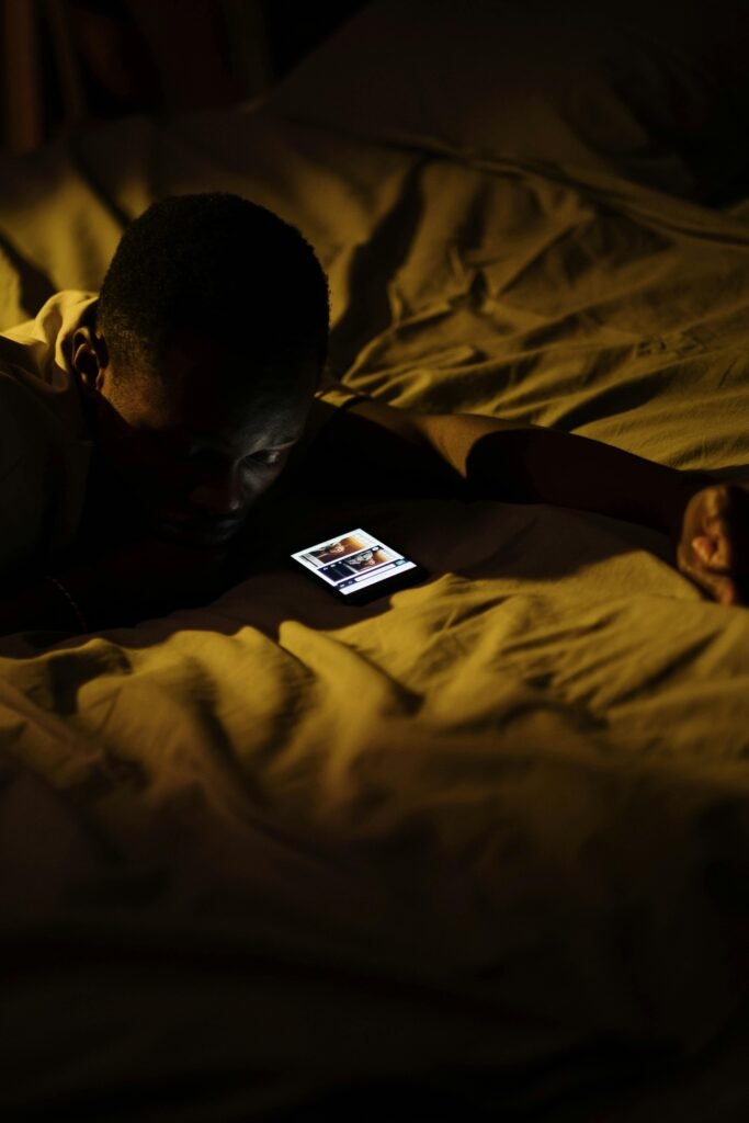 A man lying in bed at night, engaged with his smartphone, depicting sleeplessness and insomnia.